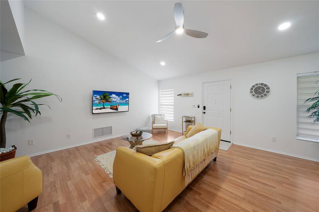 A living room with light wood floors, a yellow sofa, a wall-mounted television, and a ceiling fan — 643 MOBILE ROAD, VENICE, FL