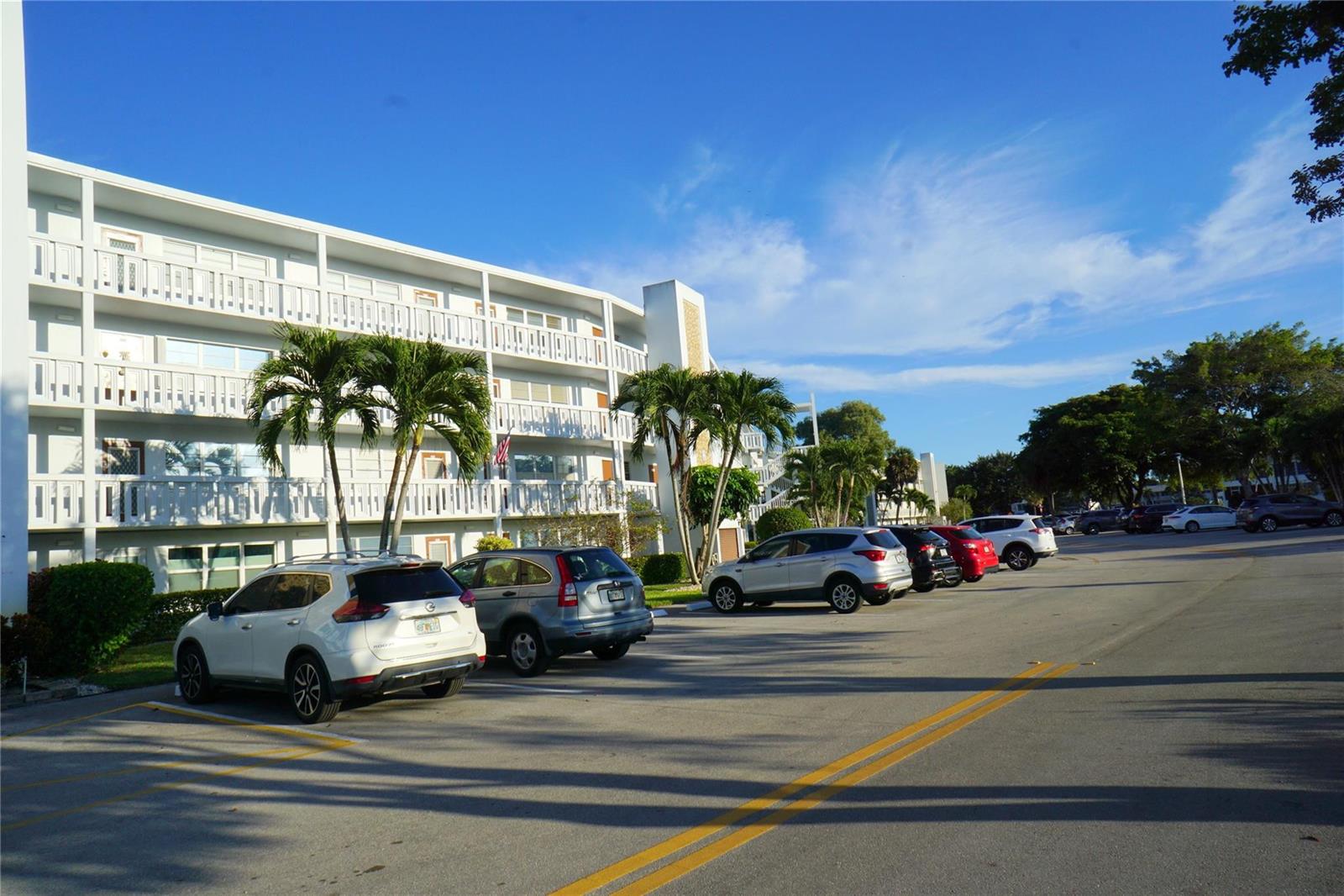 A multi-story white apartment building stands beside a parking lot with several parked cars — 4029 Newport # 4029, Deerfield Beach FL 33442, DEERFIELD BEACH, FL