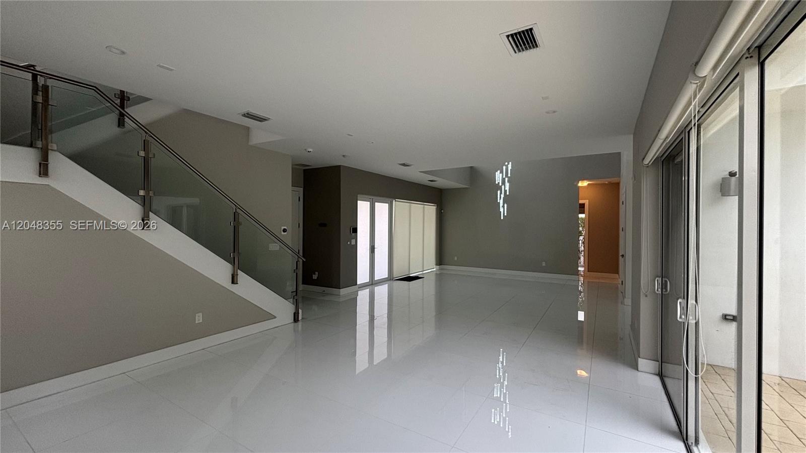 A spacious, modern living area features white tile floors, a glass-railed staircase, and sliding doors — 10108 NW 77th St # 10108, Doral FL 33178, DORAL, FL