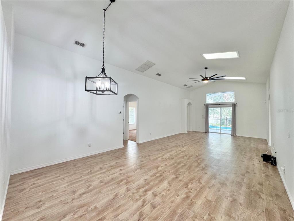 A spacious living room features vaulted ceilings, light wood-look flooring, a chandelier, and sliding doors — 502 VIOLA DRIVE, DAVENPORT, FL