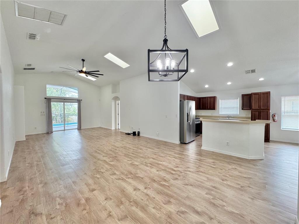 An open-concept living and kitchen area features light wood-look flooring, vaulted ceilings, and skylights — 502 VIOLA DRIVE, DAVENPORT, FL