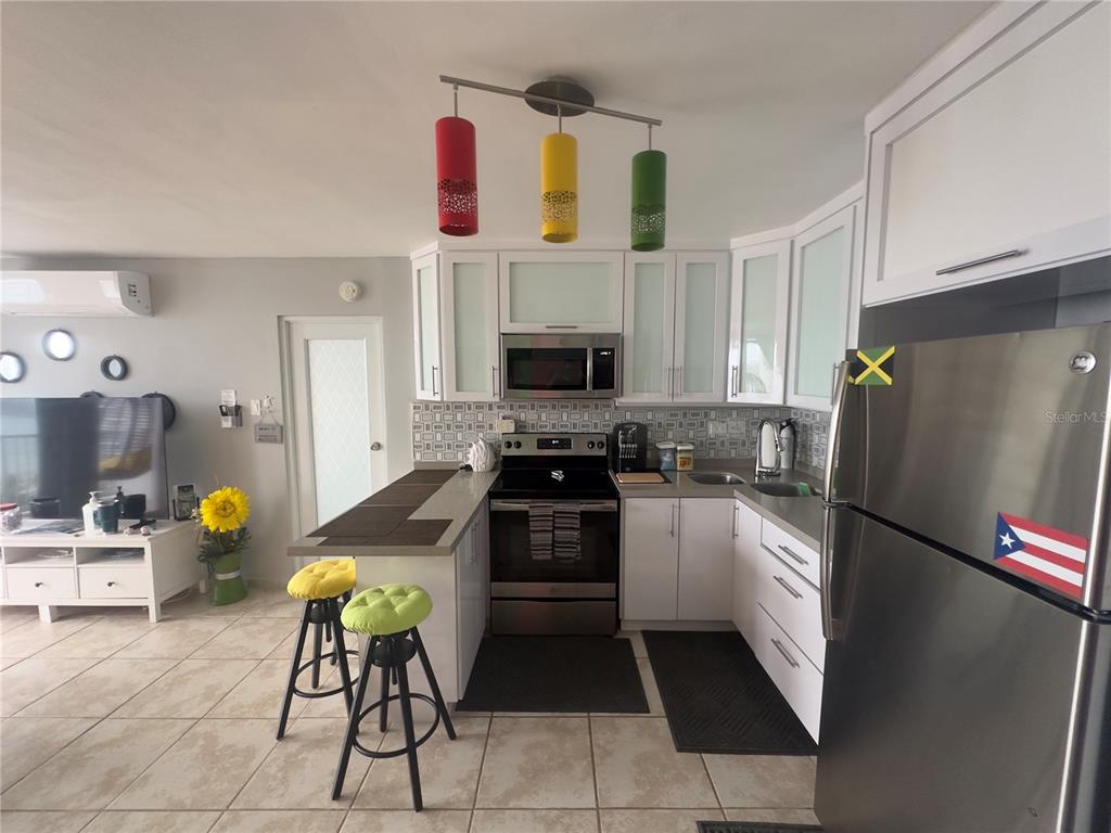 A kitchen features white cabinets, stainless steel appliances, a breakfast bar, and colorful pendant lights — Torre 1 ISLETA MARINA UNIT 10-R, FAJARDO, PR