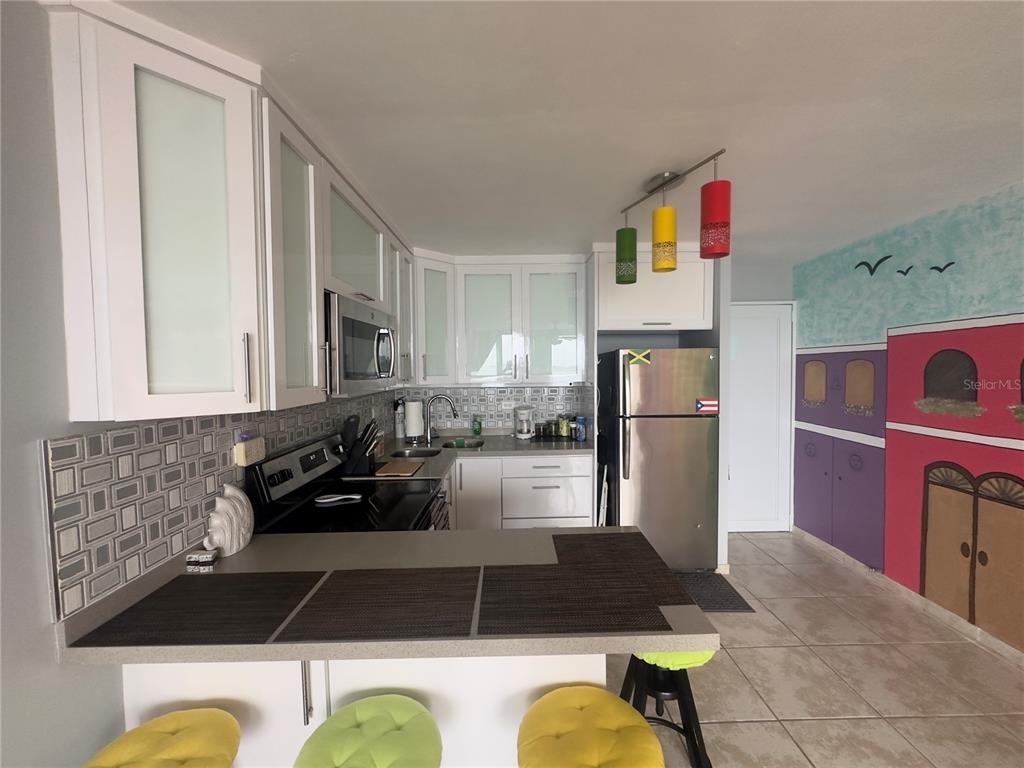 A kitchen features white cabinets, a gray tiled backsplash, stainless steel appliances, and a breakfast bar — Torre 1 ISLETA MARINA UNIT 10-R, FAJARDO, PR