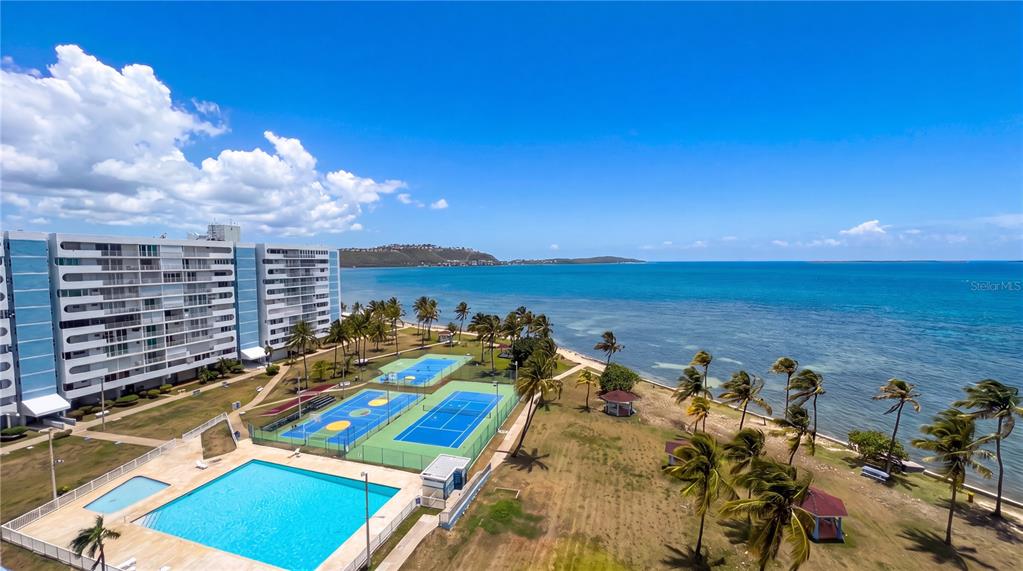 An aerial view shows a coastal apartment complex with a swimming pool and tennis courts — Torre 1 ISLETA MARINA UNIT 10-R, FAJARDO, PR