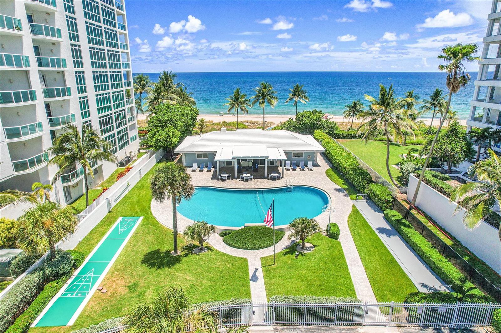 An aerial view of a swimming pool, shuffleboard court, and clubhouse beside a sandy beach — 1431 S Ocean Boulevard # 74, Pompano Beach FL 33062, POMPANO BEACH, FL
