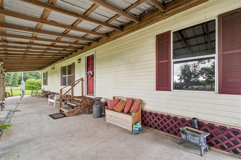 A long covered porch with a concrete floor, wooden steps, and a red front door — 4404 PLATT ROAD, PLANT CITY, FL