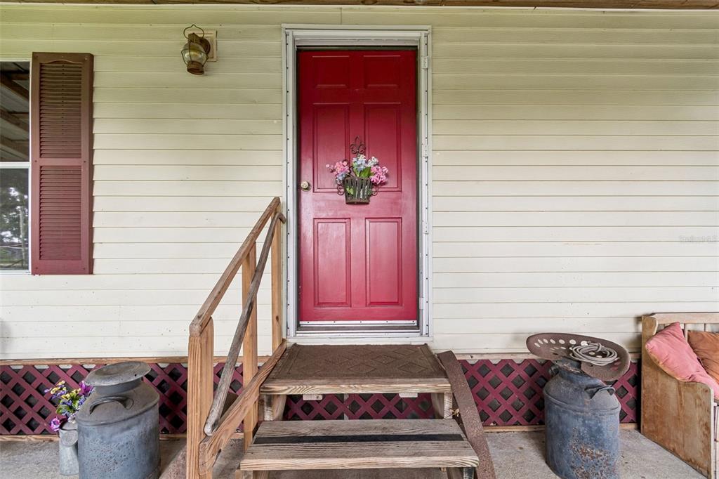 A red front door with a floral wreath is accessed by wooden steps and railings — 4404 PLATT ROAD, PLANT CITY, FL