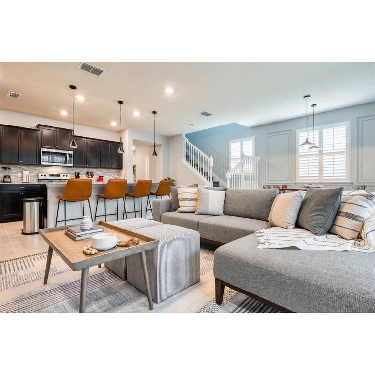 An open-concept living room features a gray sectional sofa, a coffee table, and a kitchen — 806 PARADISE DRIVE, DAVENPORT, FL