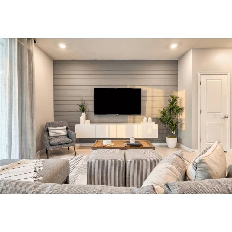 A living room features a grey shiplap accent wall, a wall-mounted white console, and furniture — 806 PARADISE DRIVE, DAVENPORT, FL