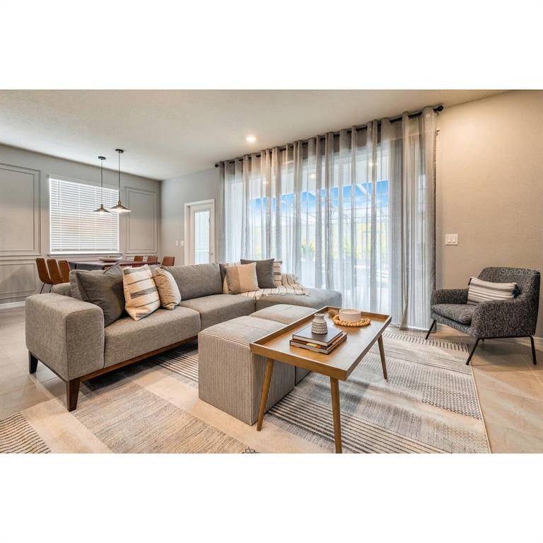 A modern living room features a gray sectional sofa, a wooden coffee table, and floor-to-ceiling curtains — 806 PARADISE DRIVE, DAVENPORT, FL