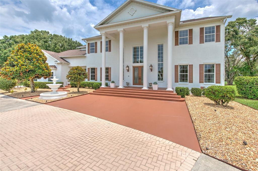 A two-story white house with a columned portico, brown shutters, and a front fountain — 11444 HAMMOCK OAKS CT, LITHIA, FL
