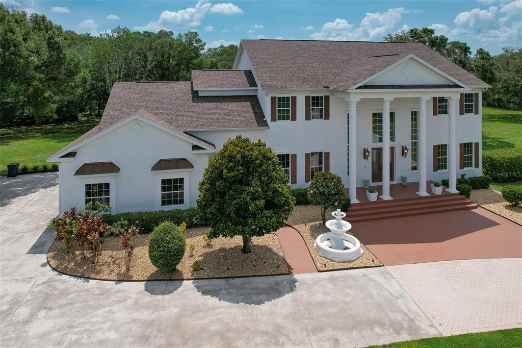An aerial view shows a two-story white house with a circular driveway and fountain — 11444 HAMMOCK OAKS CT, LITHIA, FL