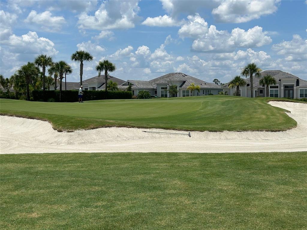 A golf course green features a sand bunker and a person putting near houses — 15983 GRASSLAND LANE UNIT 3411, PUNTA GORDA, FL