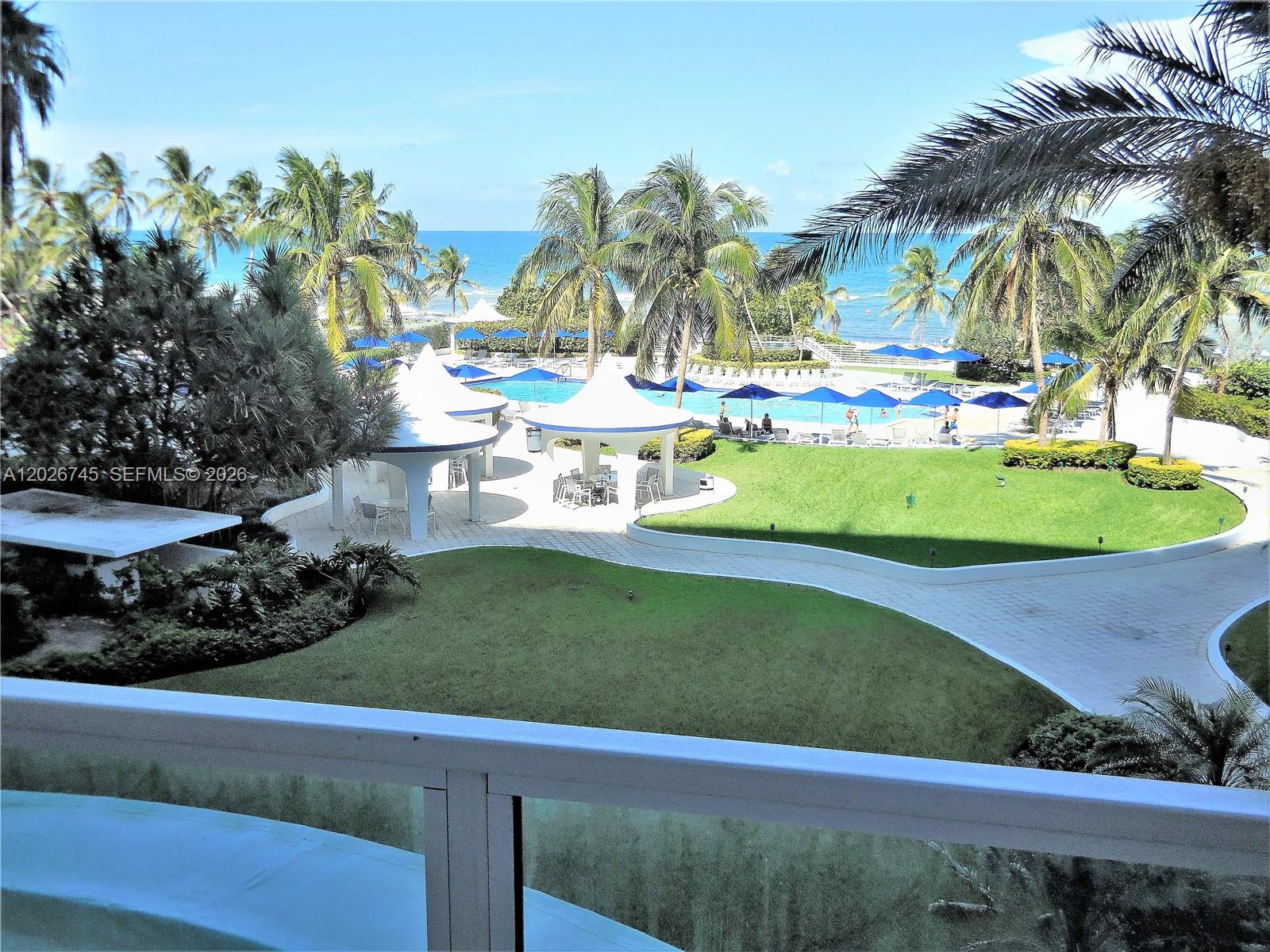 An elevated view overlooks a resort pool area with cabanas, palm trees, and the ocean — 5151 Collins Ave # 519, Miami Beach FL 33140, MIAMI BEACH, FL