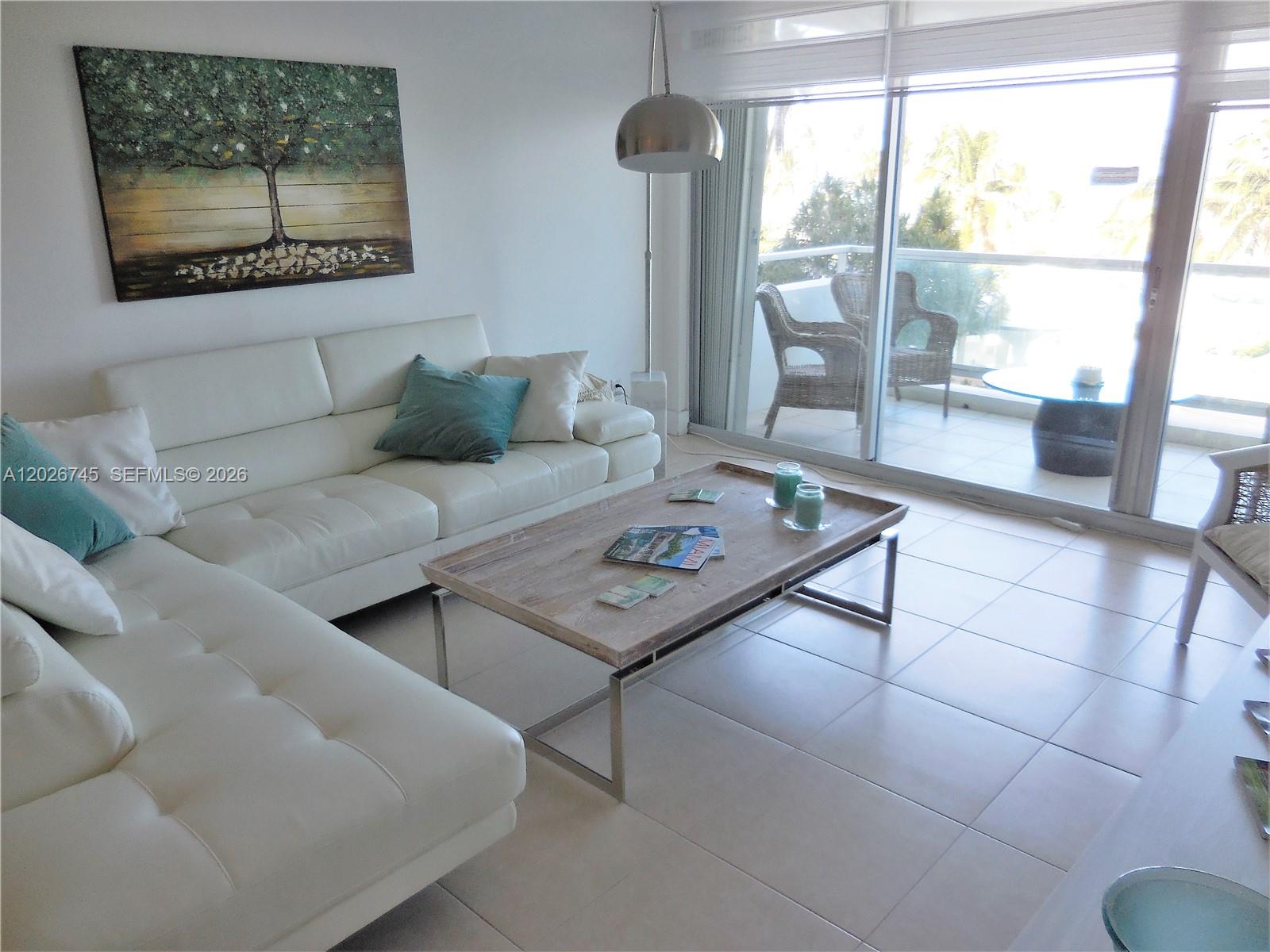A living room features a white sectional sofa, a wooden coffee table, and a balcony — 5151 Collins Ave # 519, Miami Beach FL 33140, MIAMI BEACH, FL