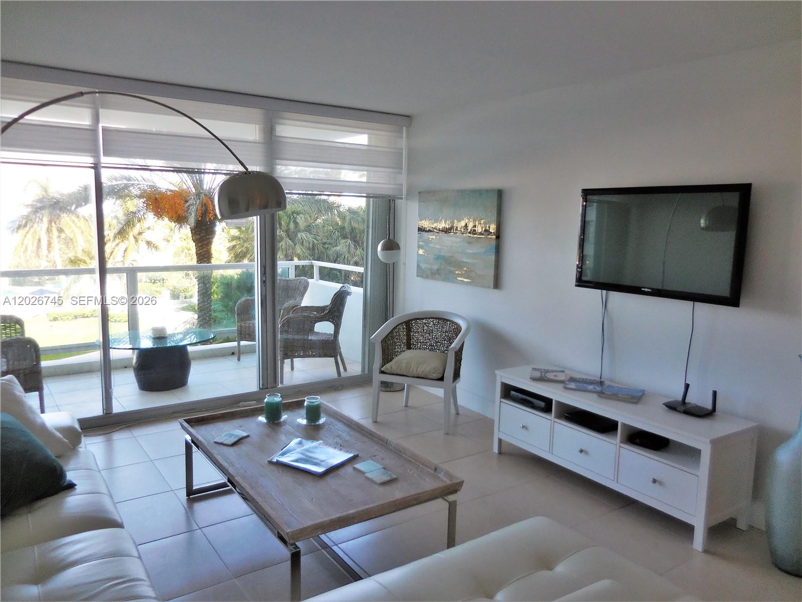 A living room features a white sofa, a wooden coffee table, and a balcony view — 5151 Collins Ave # 519, Miami Beach FL 33140, MIAMI BEACH, FL