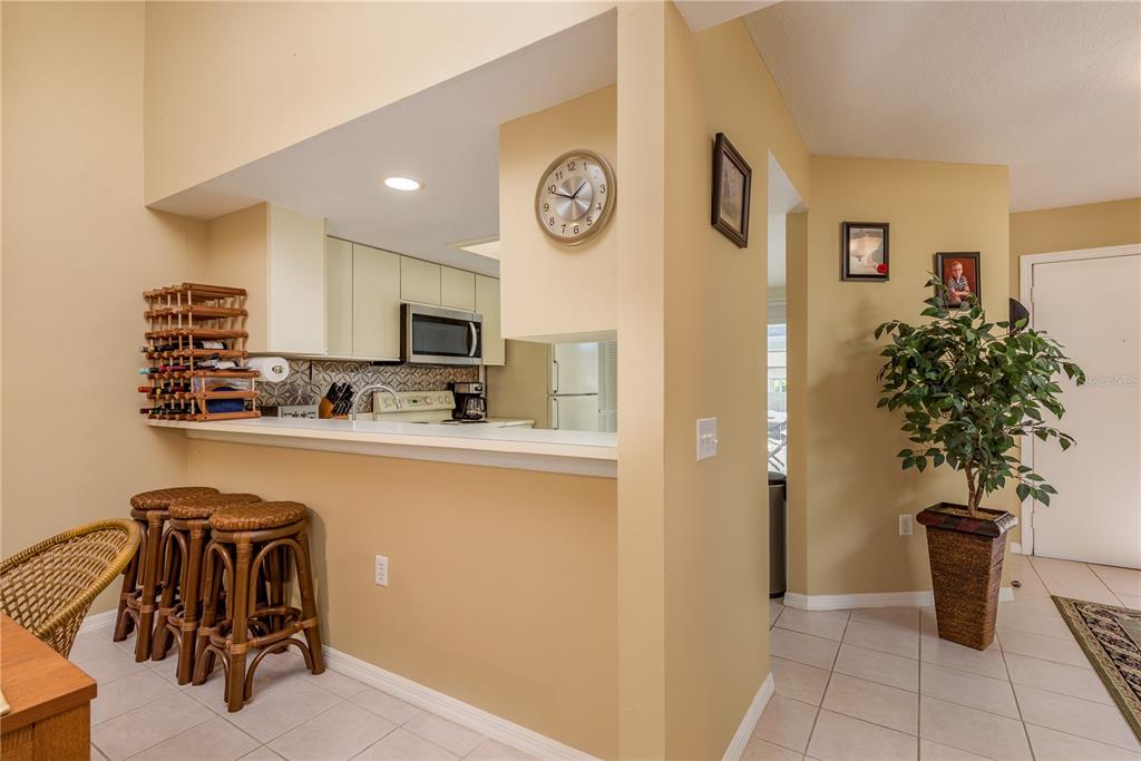 A kitchen with a breakfast bar, three stools, and a wall clock overlooks a tiled hallway — 1381 N MCMULLEN BOOTH ROAD UNIT 1381, CLEARWATER, FL
