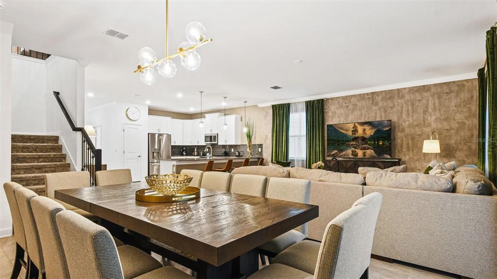 A dining area with a wooden table sits in front of an open-concept kitchen and living room — 2993 PROTAGONIST STREET, KISSIMMEE, FL
