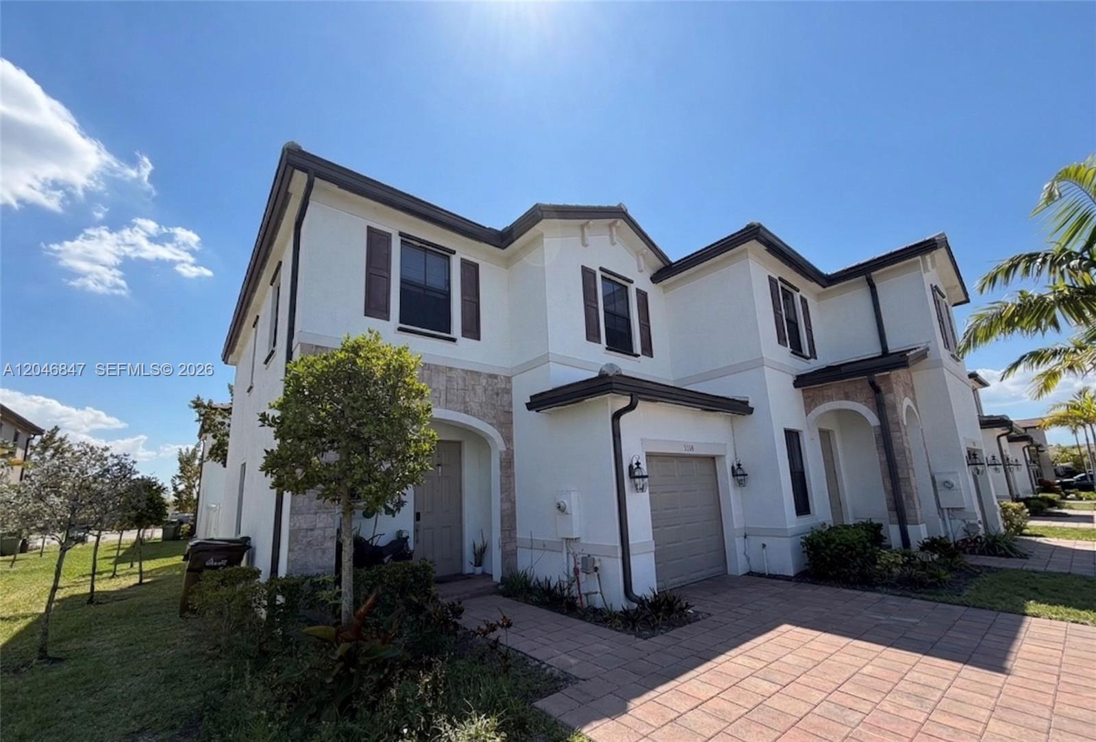 A two-story townhouse with a stone facade, beige garage, and brown shutters under a blue sky — 3338 W 112th St, Hialeah FL 33018, HIALEAH, FL