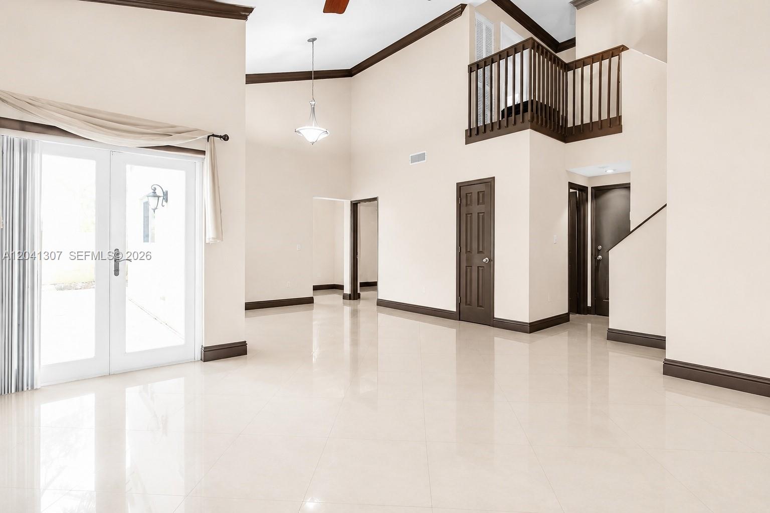 A spacious living room features high ceilings, tile flooring, dark wood trim, and a lofted balcony — 12797 NW 13th St, Sunrise FL 33323, SUNRISE, FL