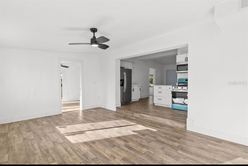 A living room with wood-look flooring leads to a raised kitchen area with white cabinets — 2360 EDNOR STREET, PORT CHARLOTTE, FL