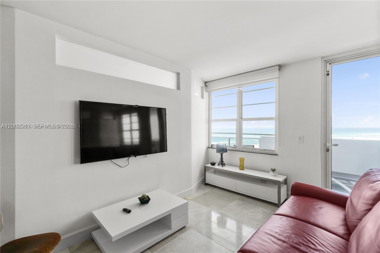 A living room features a wall-mounted television, white furniture, and a balcony with ocean views — 100 Lincoln Rd # 1046, Miami Beach FL 33139, MIAMI BEACH, FL