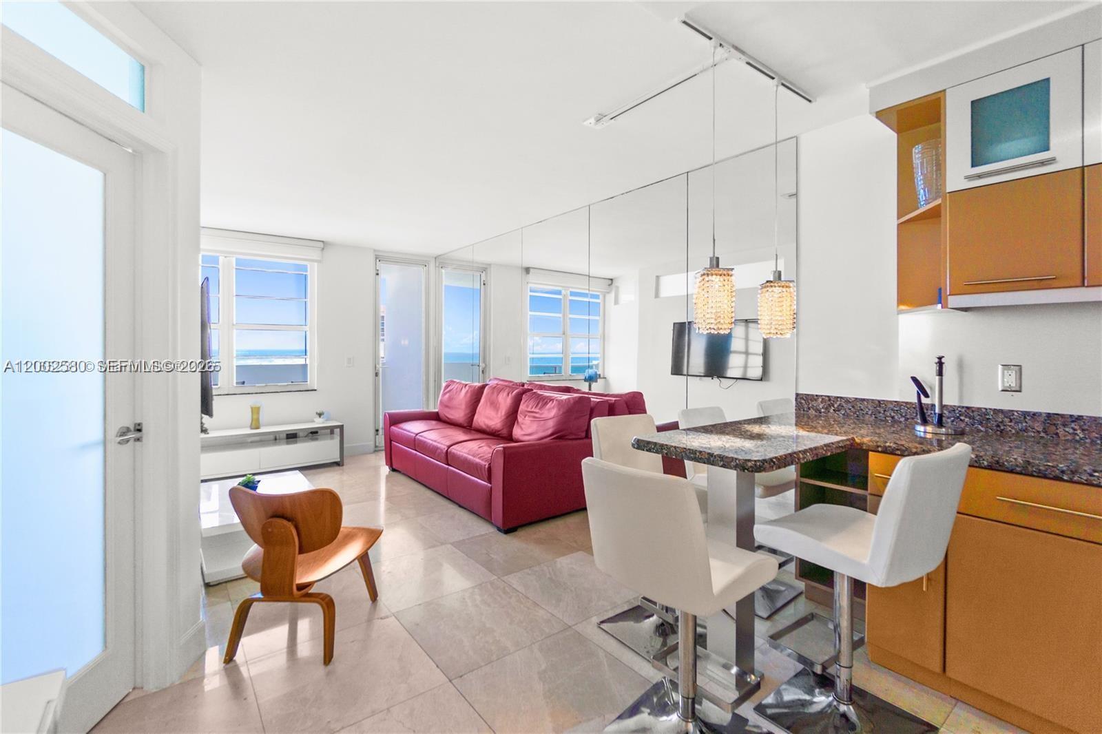 A living room and kitchen area features a red sofa, tiled floors, and mirrored walls — 100 Lincoln Rd # 1046, Miami Beach FL 33139, MIAMI BEACH, FL