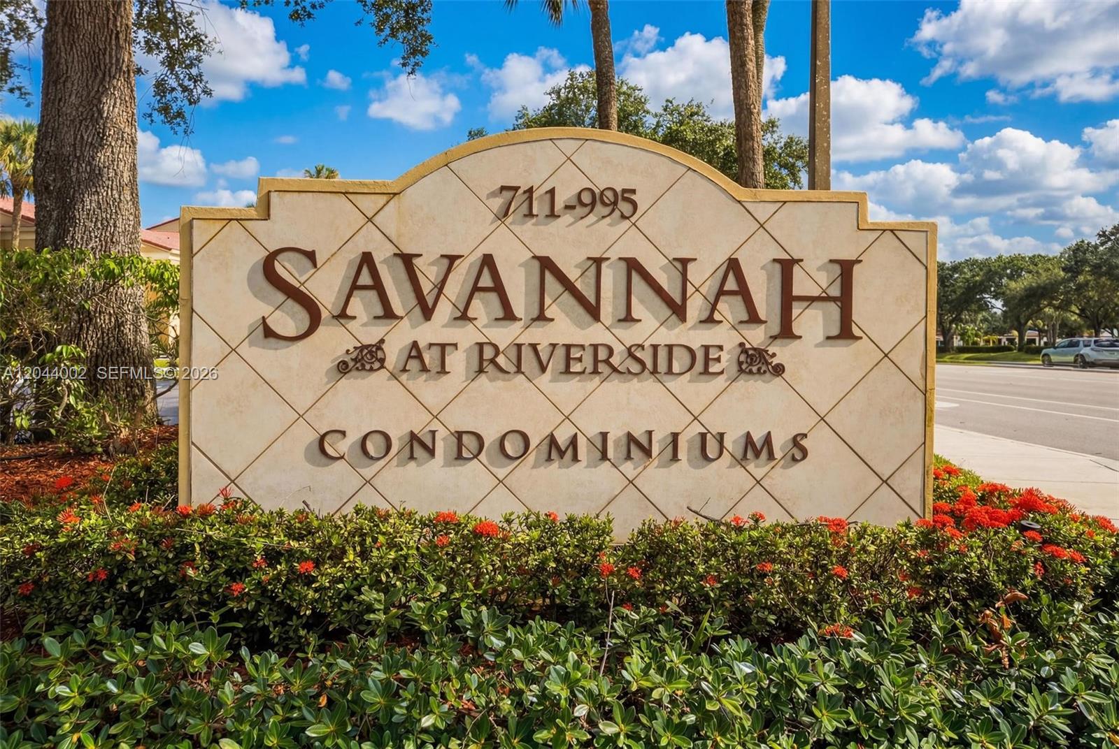 A stone sign for Savannah at Riverside Condominiums stands in a garden with red flowers — 977 Riverside Dr # 220, Coral Springs FL 33071, CORAL SPRINGS, FL
