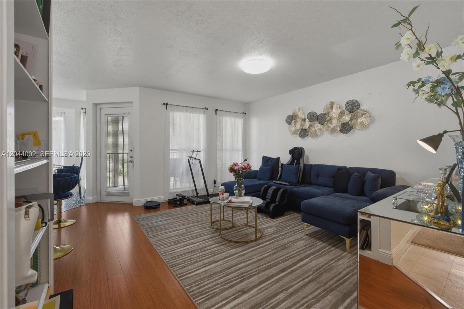 A living room features a blue sectional sofa, wood flooring, and a striped area rug — 977 Riverside Dr # 220, Coral Springs FL 33071, CORAL SPRINGS, FL