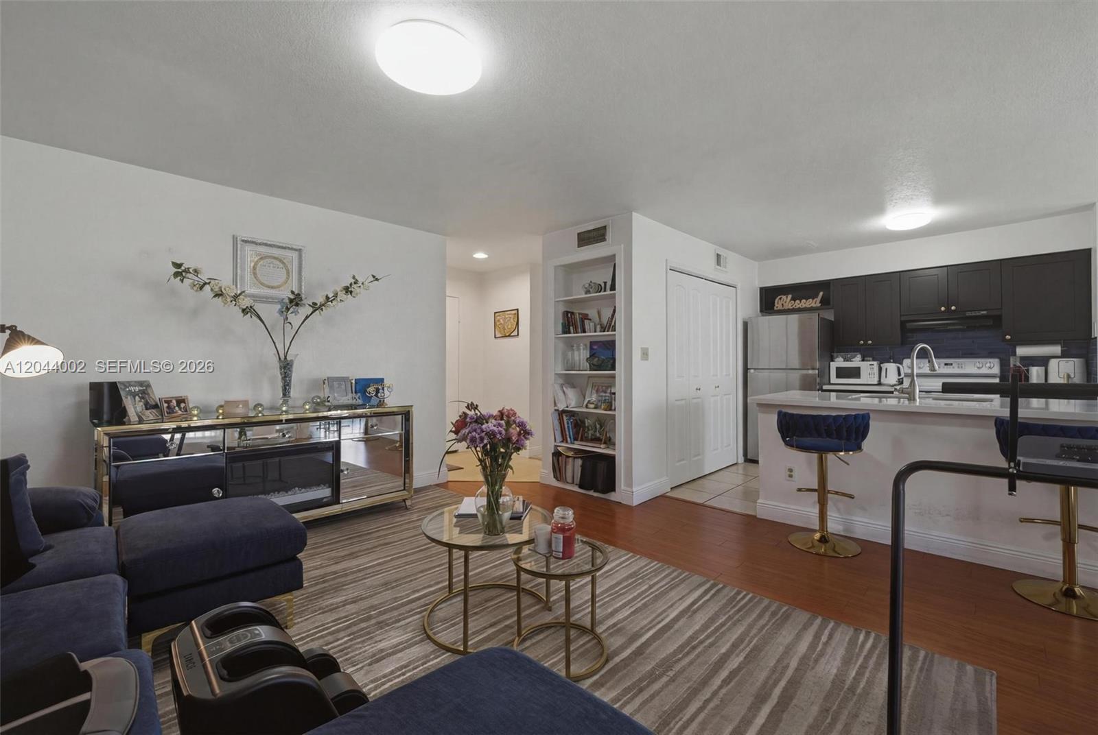A living room with a blue sofa, mirrored console, and an open kitchen with stools — 977 Riverside Dr # 220, Coral Springs FL 33071, CORAL SPRINGS, FL