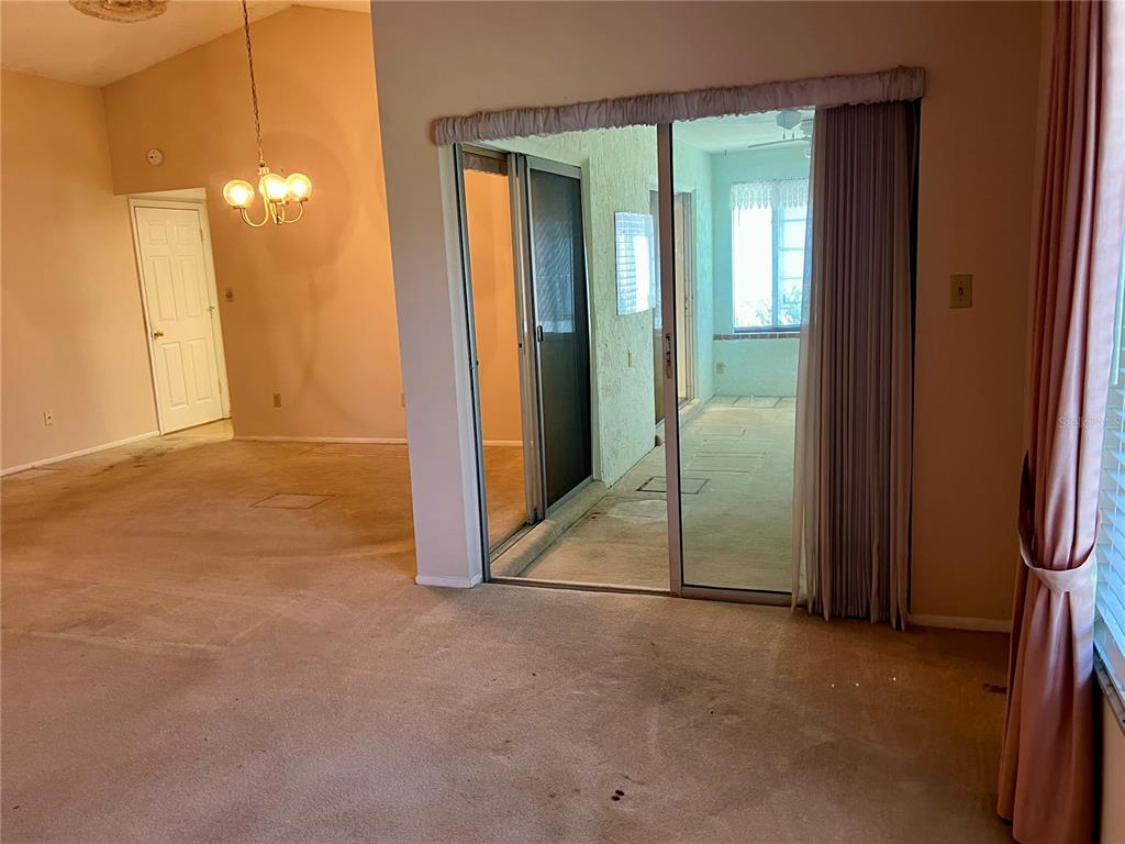 A living room with beige carpet, a vaulted ceiling, a chandelier, and sliding glass doors — 10738 LAZY LAKE DR, ORLANDO, FL