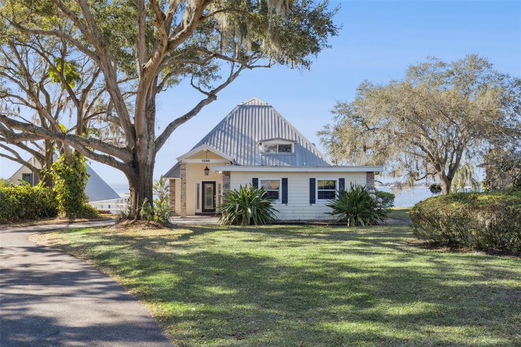 A house with a metal pyramid roof sits on a grassy lot near the water — 1280 N CROOKED LAKE DRIVE, BABSON PARK, FL