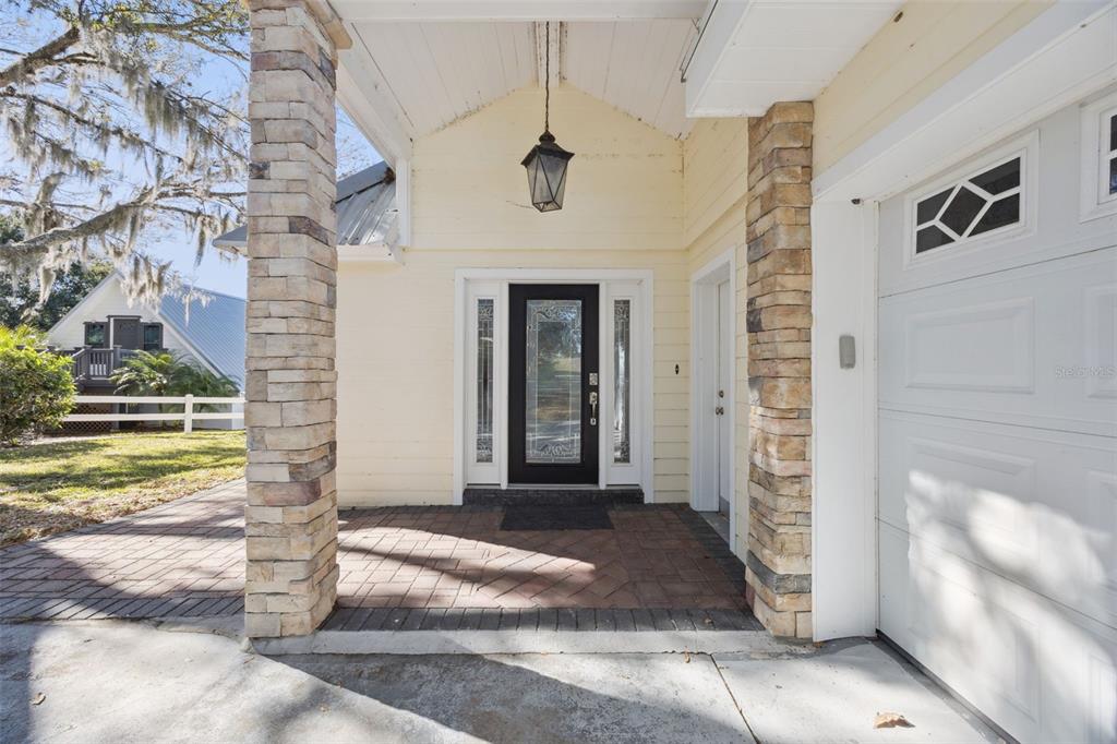 A front porch with stone pillars, a brick floor, and a black glass-paneled front door — 1280 N CROOKED LAKE DRIVE, BABSON PARK, FL