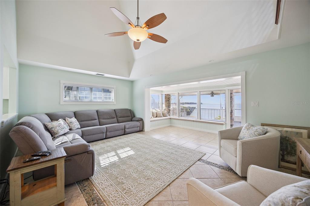 A living room features a vaulted ceiling, gray sectional sofa, and large windows overlooking water — 1280 N CROOKED LAKE DRIVE, BABSON PARK, FL