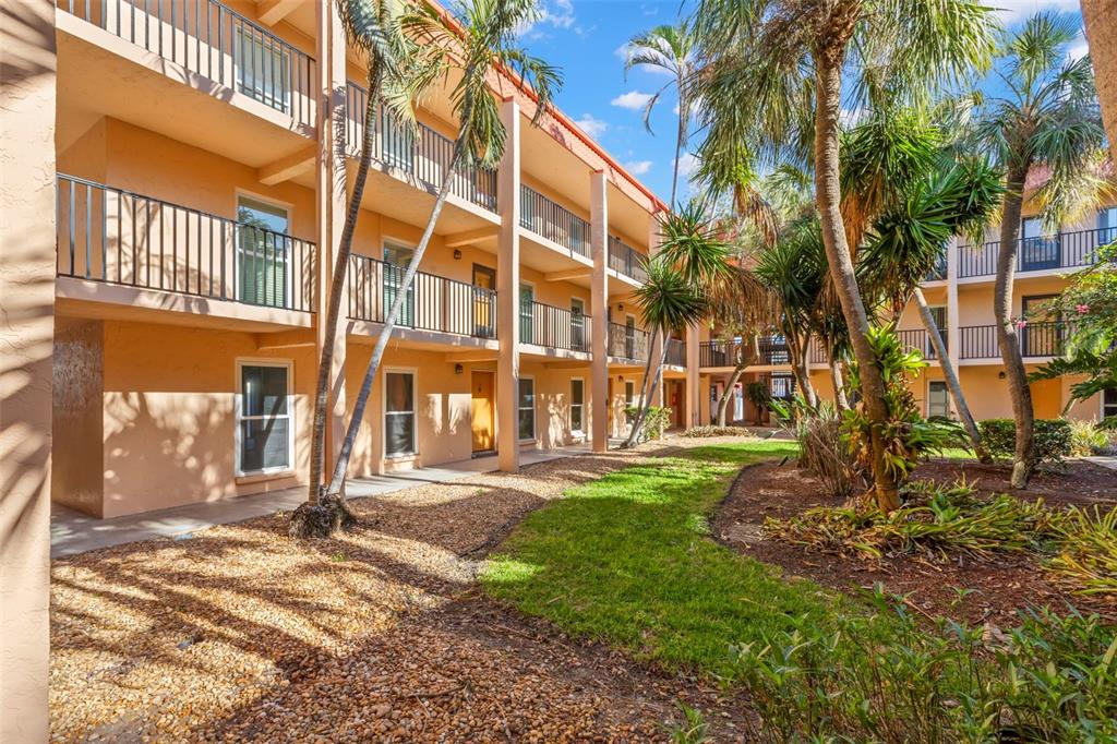 Exterior view of a three-story apartment building with balconies, palm trees, and landscaped grounds — 8911 BLIND PASS ROAD UNIT 214, ST PETE BEACH, FL