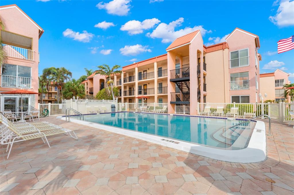 A swimming pool sits in front of a multi-story apartment building with peach-colored walls — 8911 BLIND PASS ROAD UNIT 214, ST PETE BEACH, FL