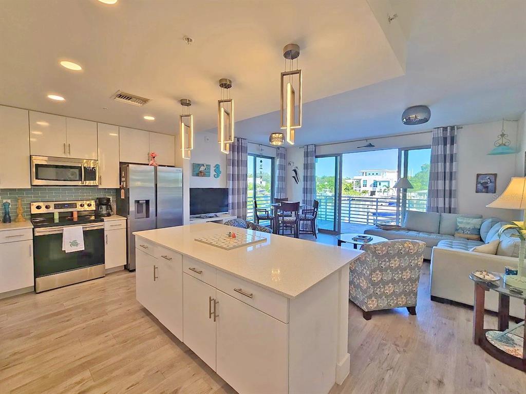 A modern open-concept kitchen and living area features a white island, stainless appliances, and balcony — 1709 N TAMIAMI TRAIL UNIT 201, SARASOTA, FL