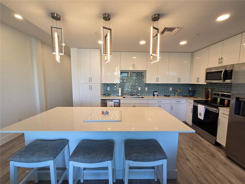 A modern kitchen features white cabinetry, a quartz island with bar seating, and blue tile backsplash — 1709 N TAMIAMI TRAIL UNIT 201, SARASOTA, FL