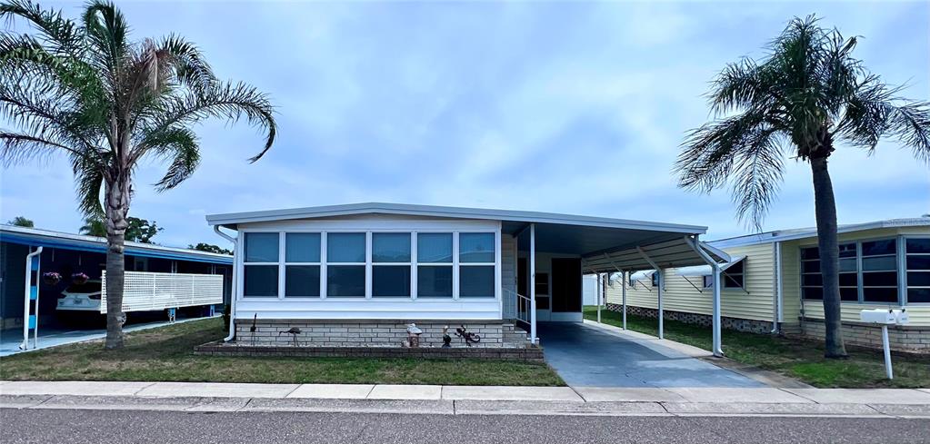 A single-story manufactured home features a white exterior, large windows, and an attached carport — 1100 BELCHER ROAD S UNIT 663, LARGO, FL