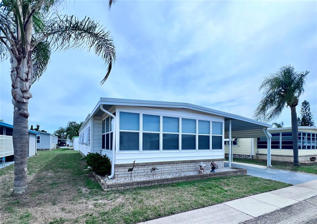 A single-story manufactured home features a white exterior, a sunroom, and a carport — 1100 BELCHER ROAD S UNIT 663, LARGO, FL