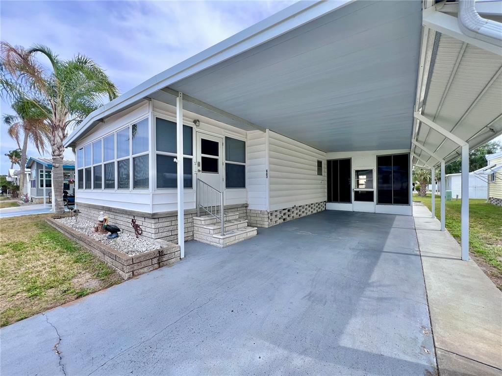 A mobile home exterior features a covered carport, a screened-in porch, and a concrete driveway — 1100 BELCHER ROAD S UNIT 663, LARGO, FL