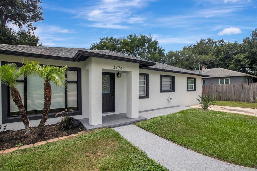 A single-story house with a white stucco exterior, dark trim, and a concrete walkway — 37743 FLORIDA AVENUE, DADE CITY, FL