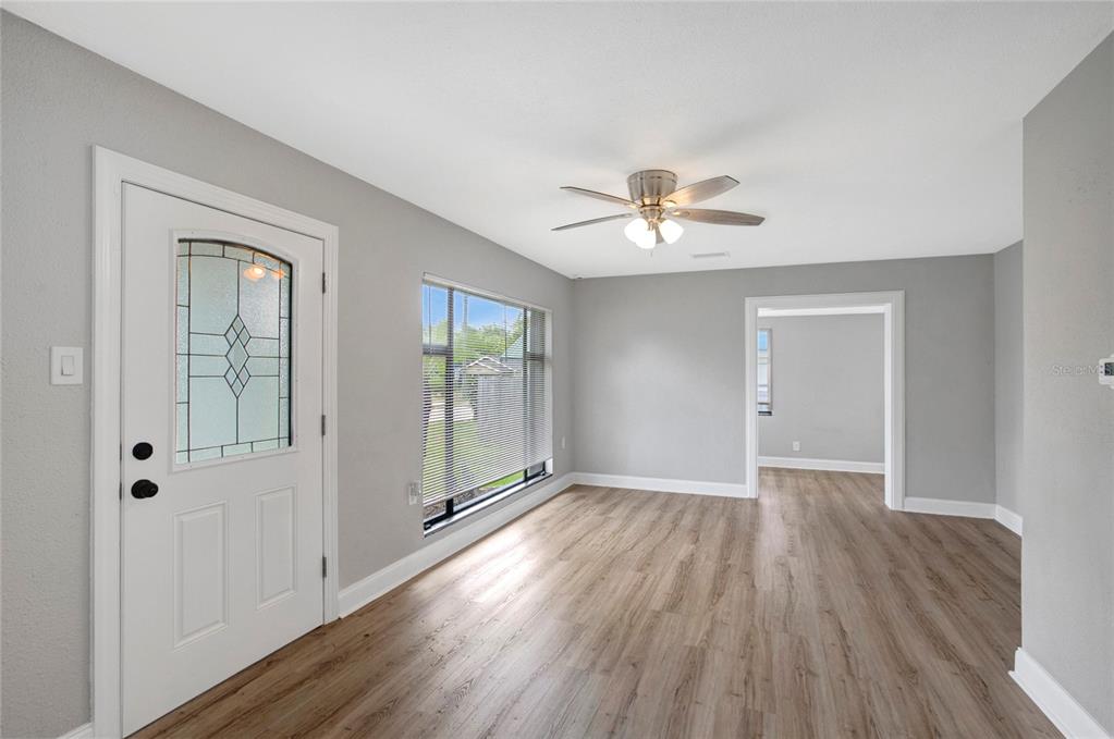 An empty room features light gray walls, wood-look flooring, a ceiling fan, and a front door — 37743 FLORIDA AVENUE, DADE CITY, FL