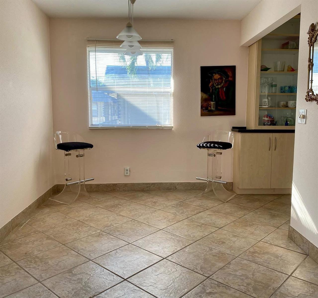 A dining area features tile flooring, two clear bar stools, a window, and a built-in cabinet — 568 Brittany L, Delray Beach FL 33446, DELRAY BEACH, FL