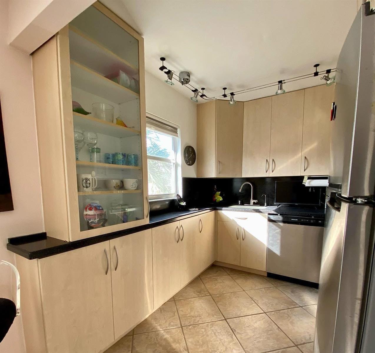 A kitchen features light wood cabinets, black countertops, stainless steel appliances, and track lighting — 568 Brittany L, Delray Beach FL 33446, DELRAY BEACH, FL