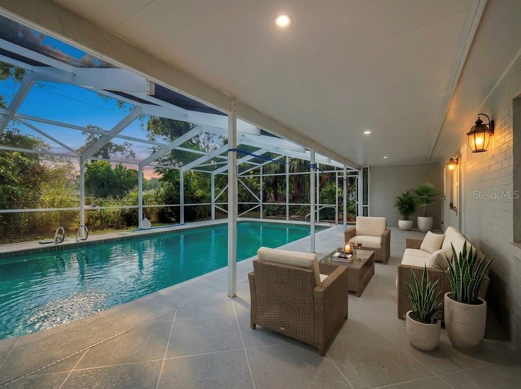 A covered patio with outdoor furniture overlooks a screened-in swimming pool at sunset — 605 WILLIAMSBURG DRIVE, DAYTONA BEACH, FL