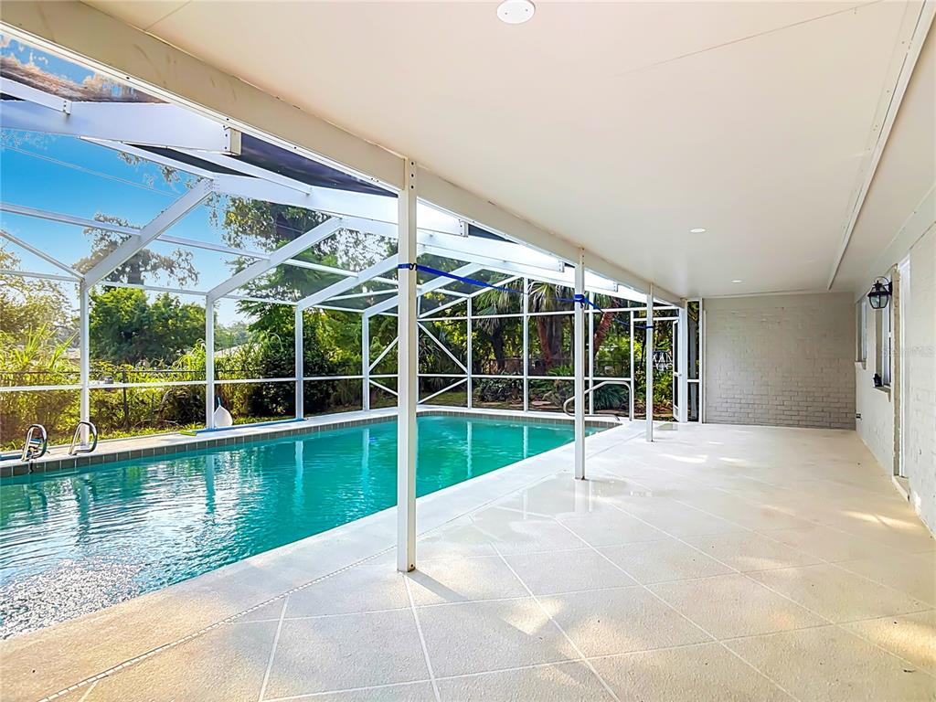A covered patio with a tiled floor overlooks a swimming pool enclosed by a screen — 605 WILLIAMSBURG DRIVE, DAYTONA BEACH, FL