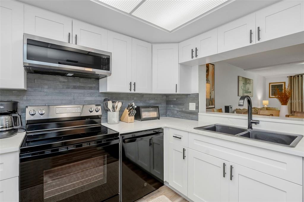 A kitchen features white cabinets, stainless steel appliances, a gray stone backsplash, and a sink — 2614 COVE CAY DRIVE UNIT 102, CLEARWATER, FL