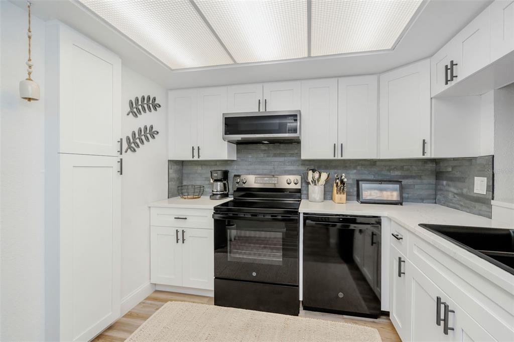 A kitchen features white cabinets, black appliances, a gray tiled backsplash, and a drop ceiling — 2614 COVE CAY DRIVE UNIT 102, CLEARWATER, FL