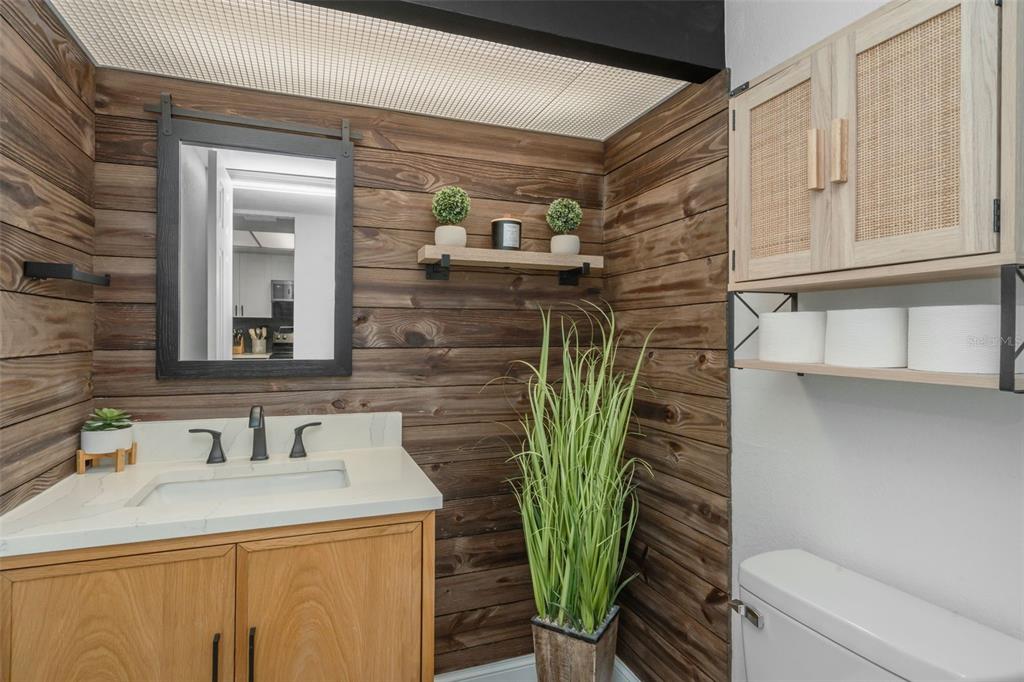 A bathroom features wood-paneled walls, a light wood vanity, and a wall-mounted cabinet with shelving — 2614 COVE CAY DRIVE UNIT 102, CLEARWATER, FL